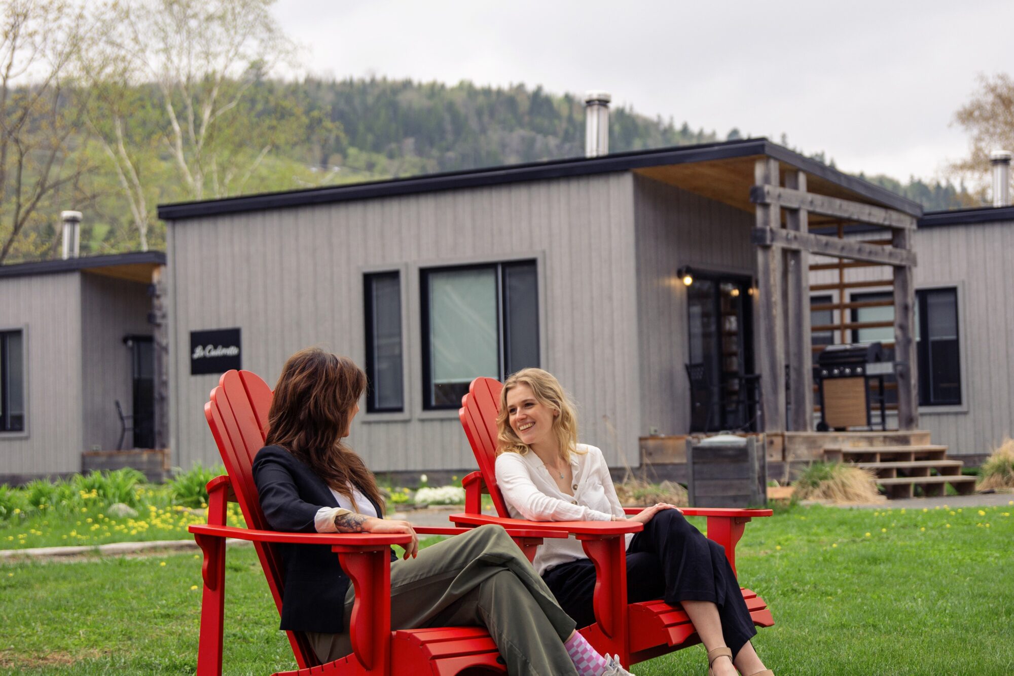 Deux femmes assises sur des chaises adirondak devant les chalets du 2800 du Parc.
