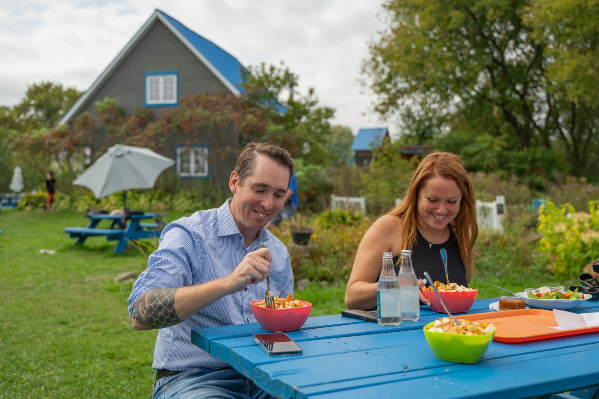 Couple qui mange une poutine fermière sur une table de pique-nique à la ferme Les Couleurs de la terre.