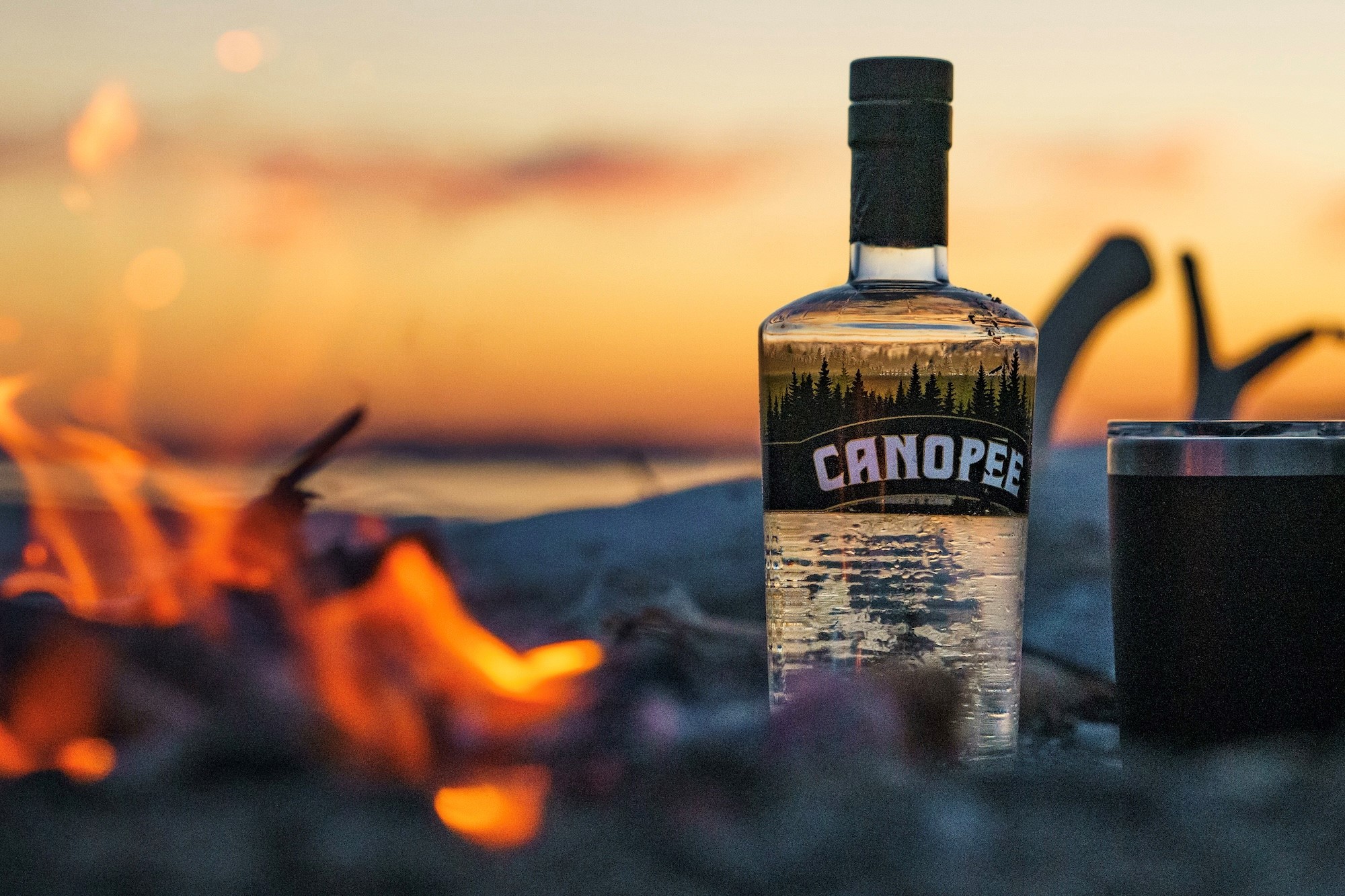 Bouteille de gin Canopée près d'un feu de camp sur une plage