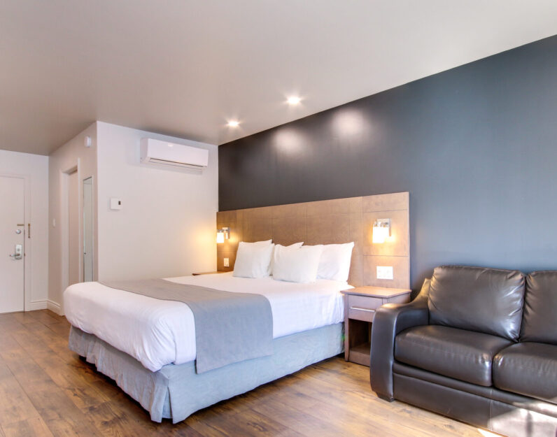 Chambre de l'Hôtel Marineau avec un grand lit, un bureau de travail et un fauteuil deux places.