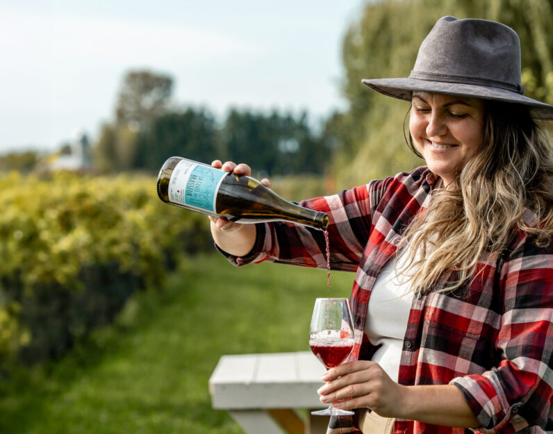 Femme qui rempli un verre de vin devant les vignes au Vignoble et Domaine Beauchemin