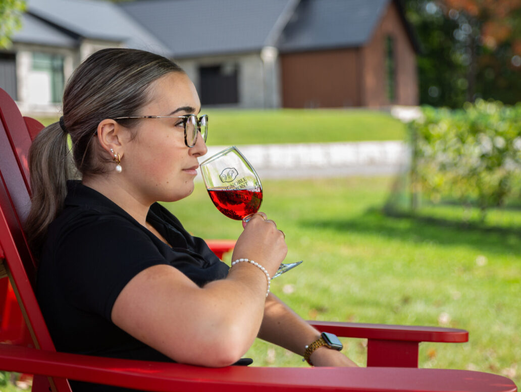 Femme qui déguste un verre de vin, assise sur une chaise adirondak en face des vignes
