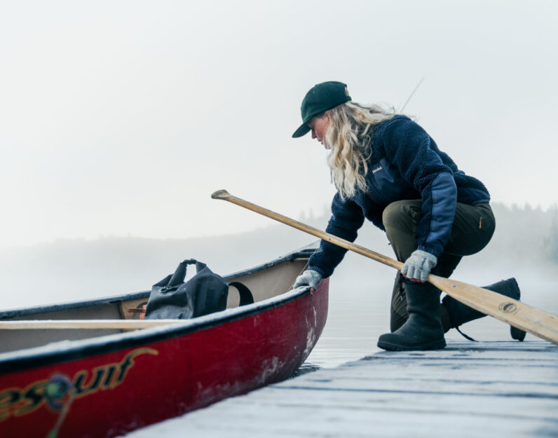 Femme qui embarque dans son canot devant un lac brumeux en automne à La Tuque