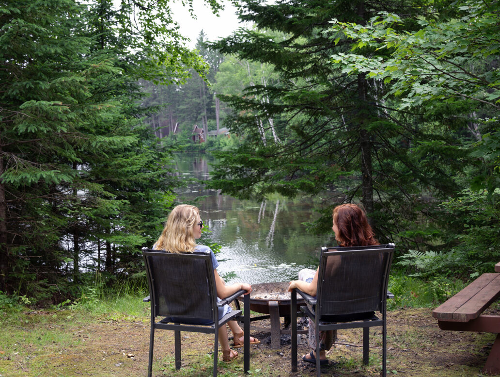 Deux femmes assises devant un foyer et un lac au Domaine Tavibois